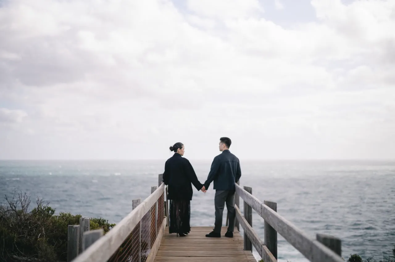 Vivi and Max holding hands on a wooden lookout above the sea